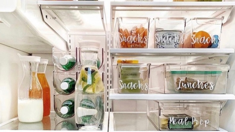 Refrigerator organized with clear storage bins that have white labels on the outside