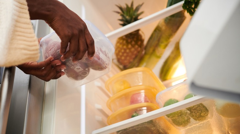 Woman holding a container of food as she organizes the refrigerator
