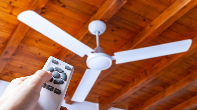 hand holding remote control and pointing it at ceiling fan