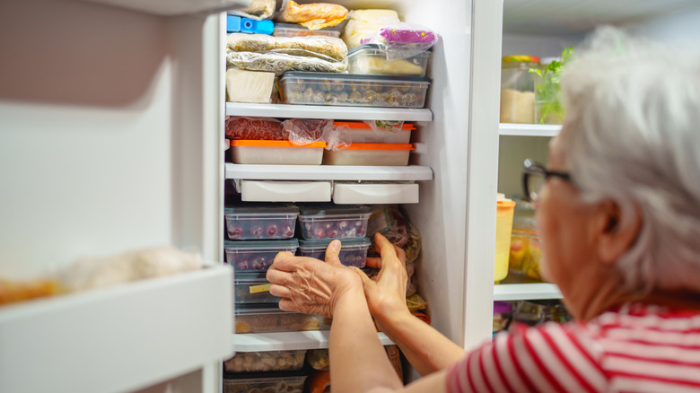 elderlysenior lady taking out package from standing freezer