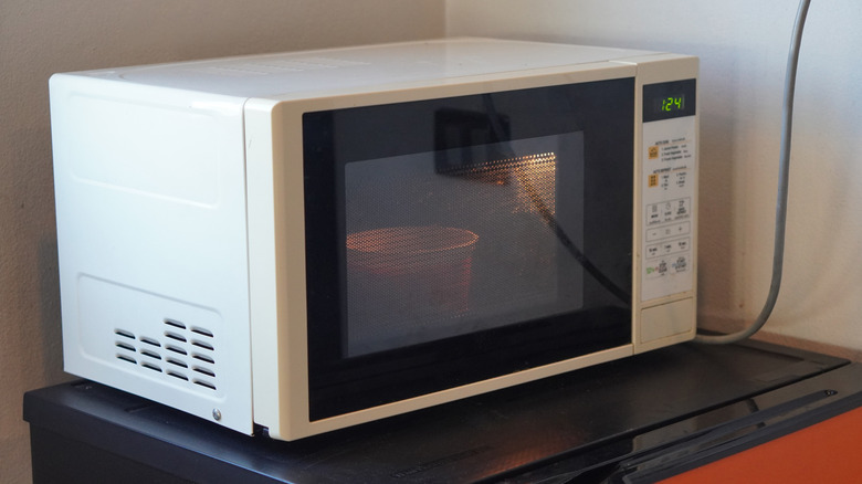 old white microwave in use on top of red fridge