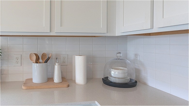 White farmhouse cabinets and Corian counter tops with kitchen utensil holder and glass dome cloche