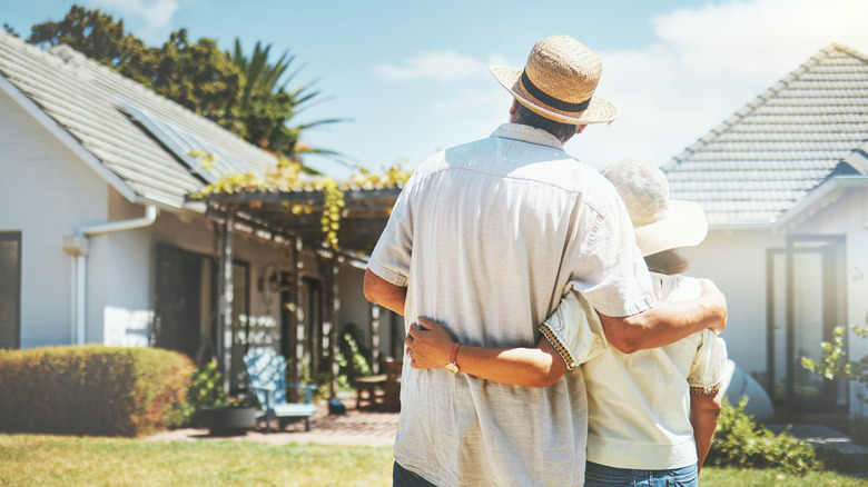 Backview of couple hugging in front of their new home on bright day