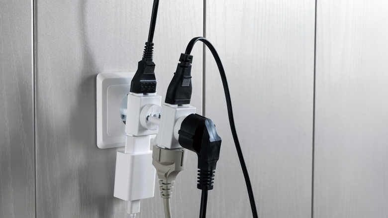 Multiple plugs connected to one electric outlet on gray wall