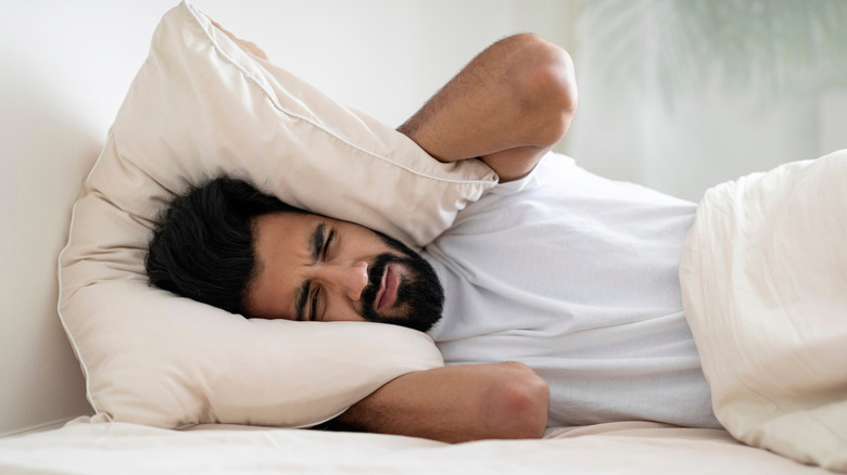 Man in bed covering his head with a pillow due to noise