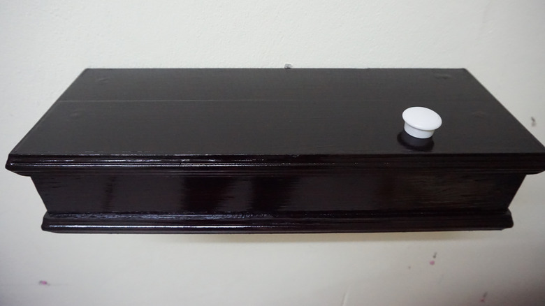 A decorative shelf with a hidden compartment inside and decorative pull on surface