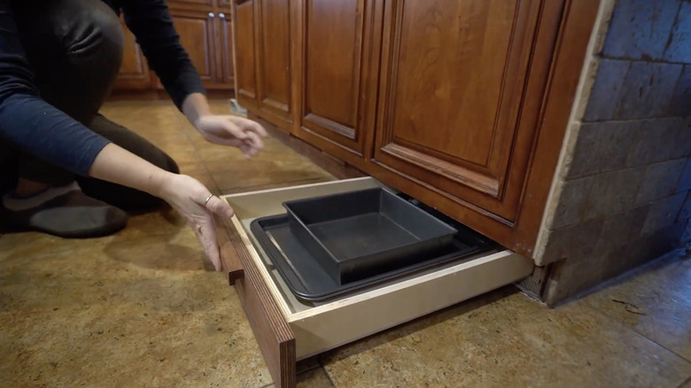 A person storing baking trays in a toe-kick cabinet
