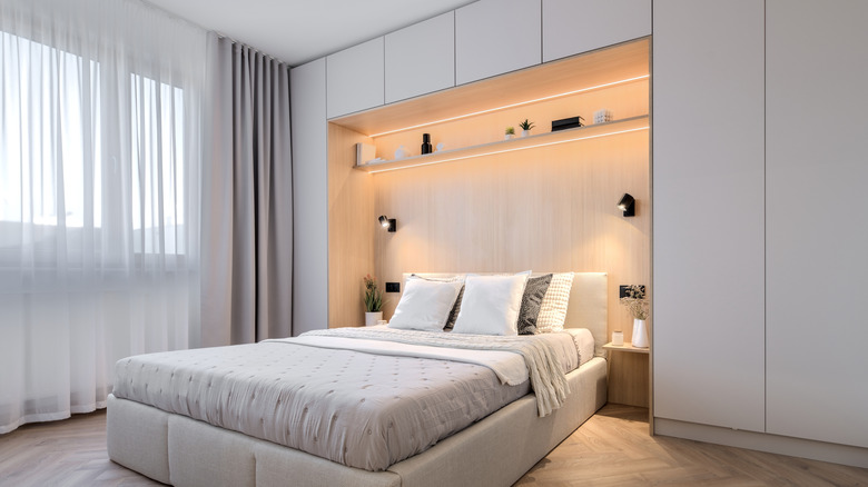 A modern bedroom with cabinets and shelving wrapping around the headboard area of the bed