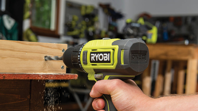 Hand using Ryobi tool to drill into wood with other Ryobi tools in the background