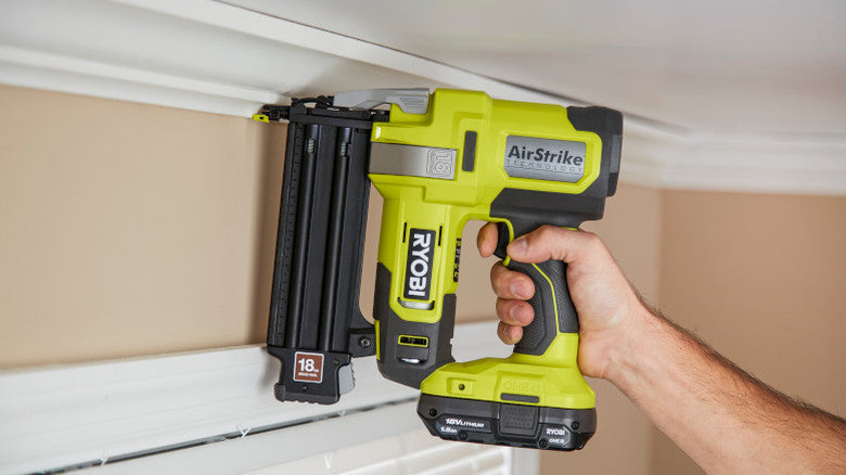 Hand holding Ryobi ONE+ Cordless AirStrike Brad Nailer and using it on crown molding