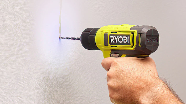 Hand holding the Ryobi 18V ONE+ Drill and drilling a hole into a wall