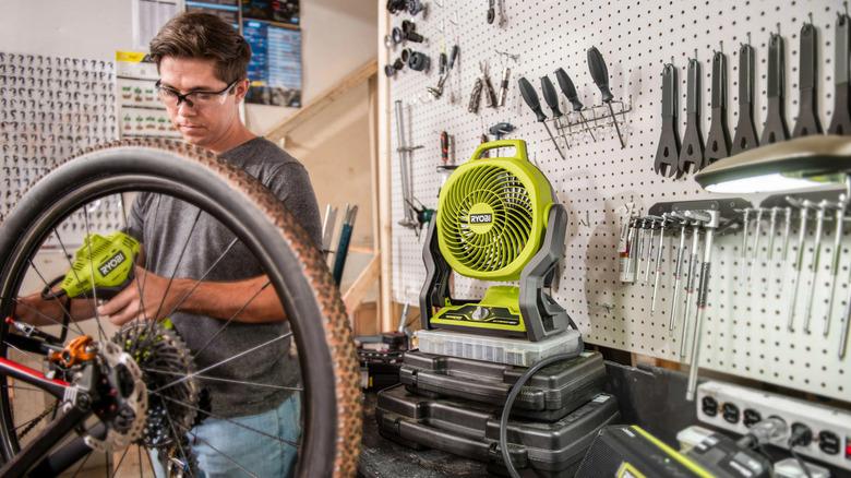 Man working in garage with Ryobi ONE+ Whisper Series Fan on a work table