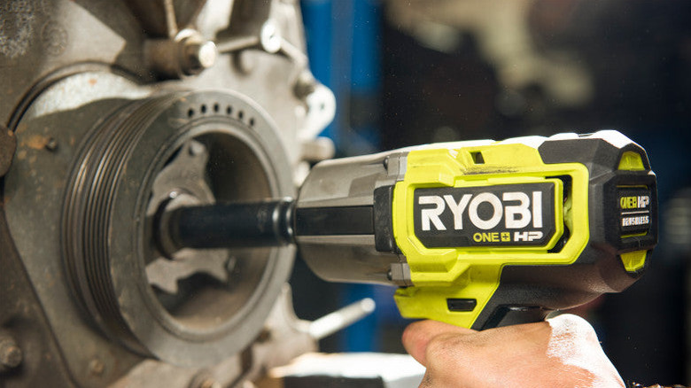 Hand holding impact wrench to remove bolt from machine