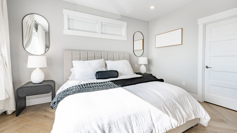 Two oval mirrors hanging on a bedroom wall beside the bed
