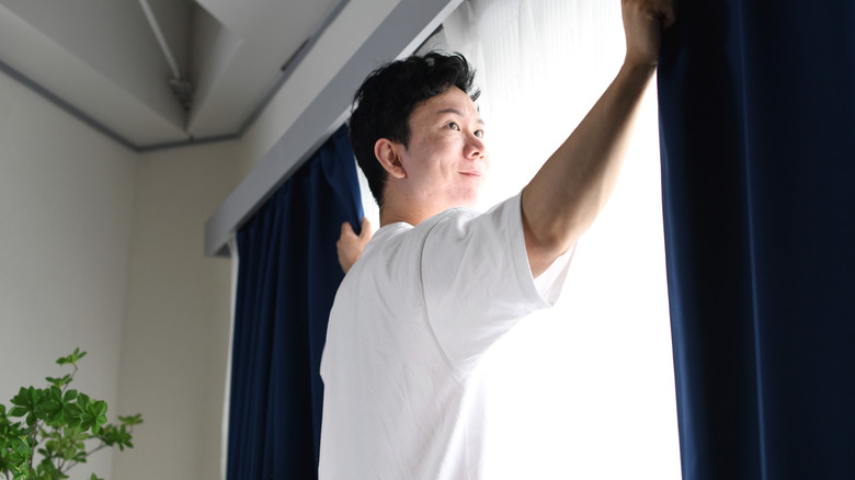 Person pulling blackout curtains closed