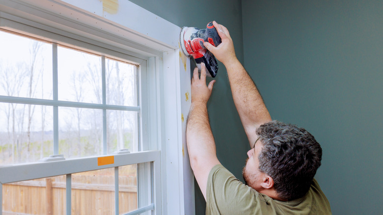 Man sanding window trim in preparation for painting