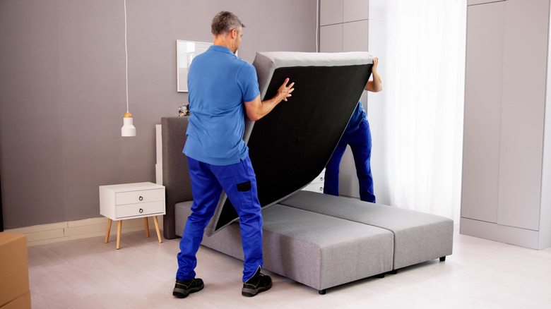 People lifting a mattress in a bedroom