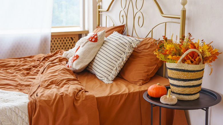 Cozy rich orange and beige bedding with throw pillows and autumnal decor