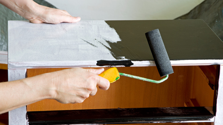 Person using a roller to paint a dresser