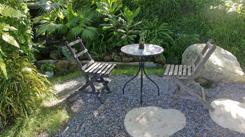 Small table surrounded by high plants on a gravel patio