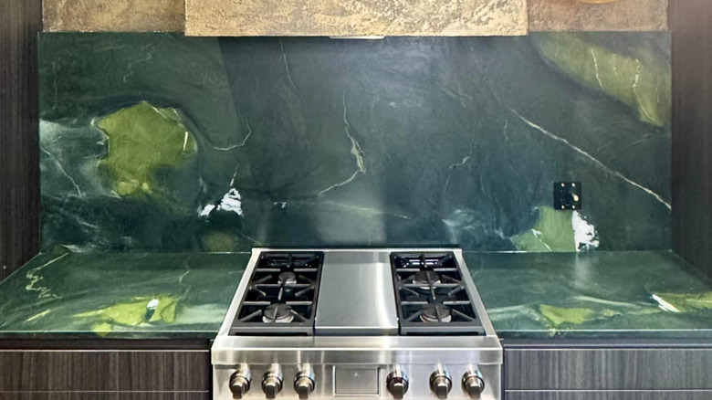 A dark green backsplash with a gold oven hood.