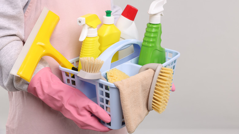 Gloved hands holding a basket of cleaning supplies
