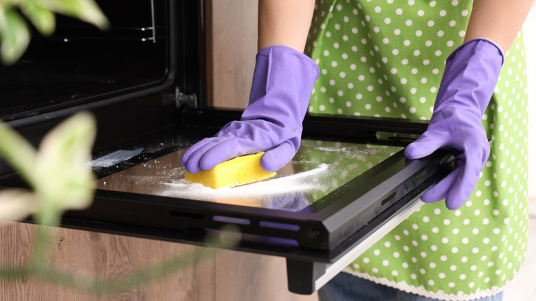 Person wearing purple gloves cleaning the door of an oven