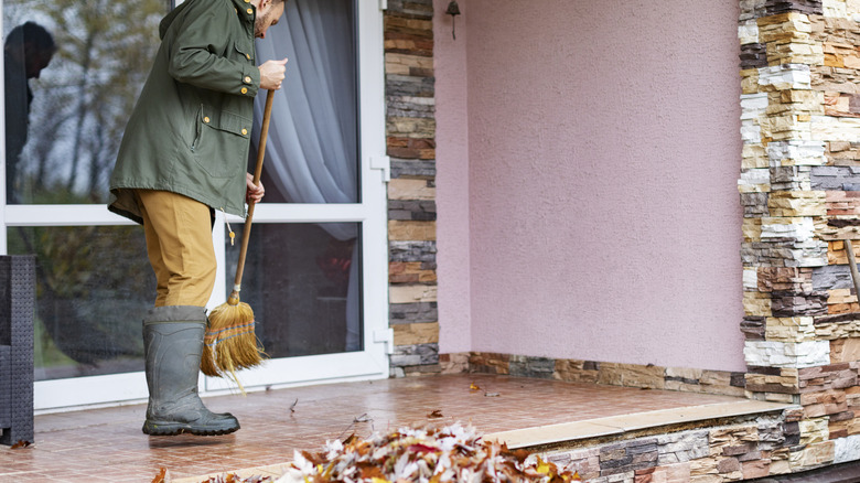 Man sweeping leaves off porch