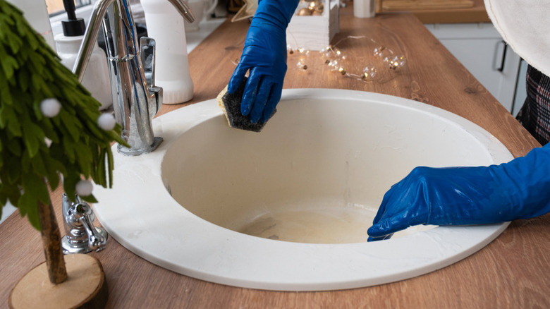 Gloved hands cleaning sink next to string lights and mini holiday tree