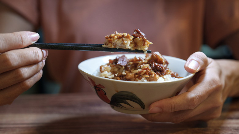 Hands lifting rice out of bowl with chopsticks