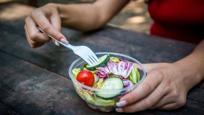 Person eating salad with plastic fork