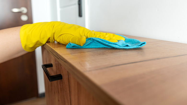 Person cleaning a faux wood cabinet or desk with a rag