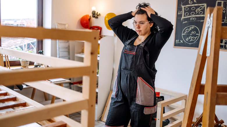 A woman looking stressed while looking at wood furniture in her workshop