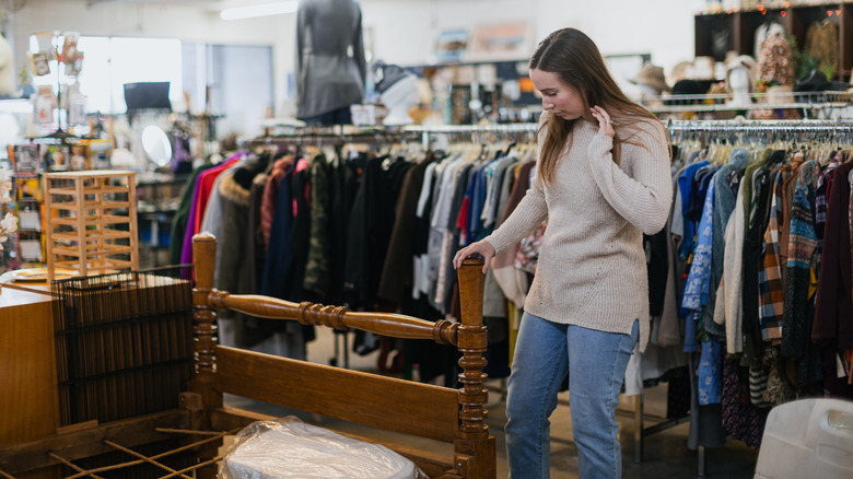 A woman looking at a wood bed frame in a thrift store