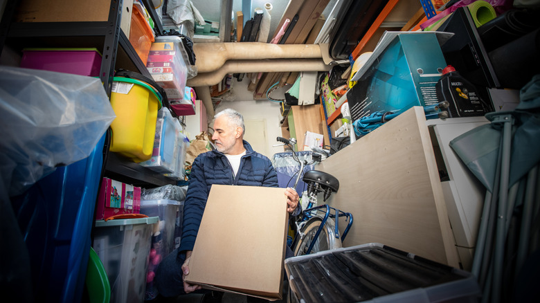 Older man carrying a box and looking at storage shelves with other containers on them