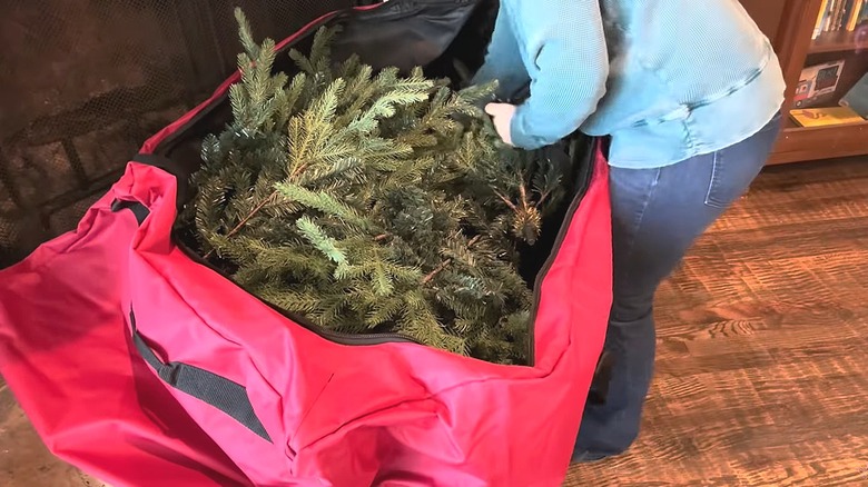 Woman packing an artificial Christmas tree into a red rolling tree storage bag