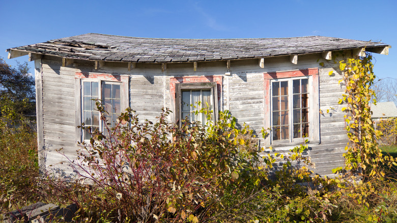 A small old gray cottage with a sagging roof deck and missing shingles