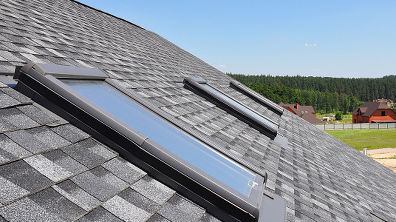 A gray roof with three skylights against a blue sky