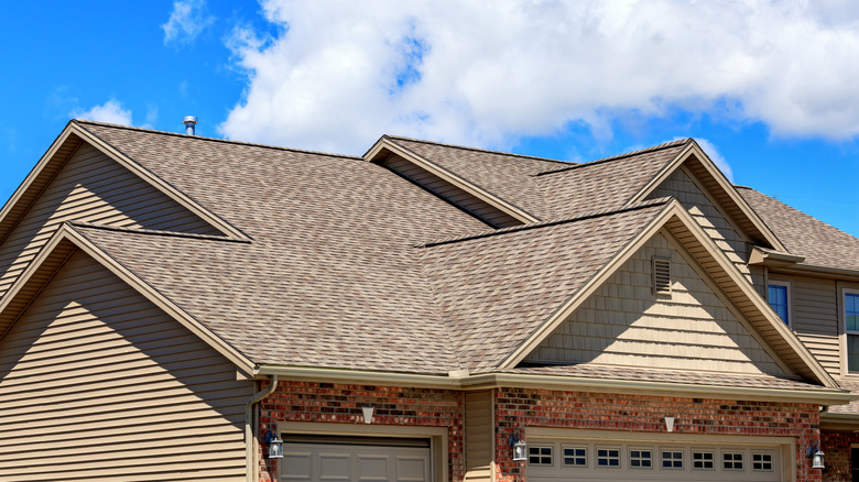 BRonw shingles on a beige suburban home against a blue sky with white clouds