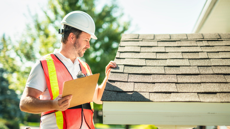 A roof inspector holds a clipboard while checking out a roof