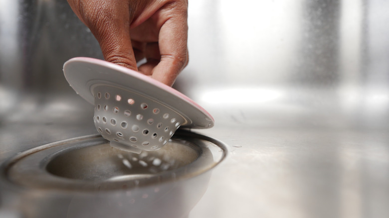 person removing sink strainer from sink drain