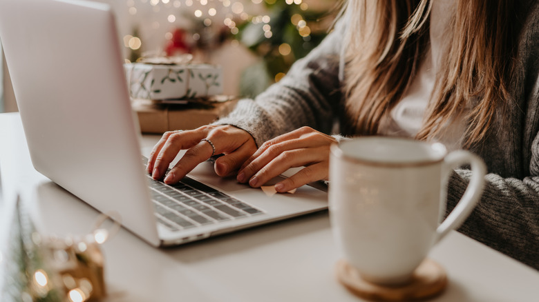 Woman using computer in a cozy home with hot drink