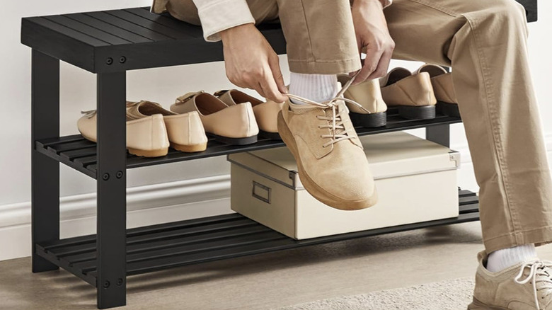 Person sitting on bamboo shoes rack, putting on shoes
