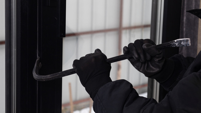 Hands using a crow bar to pry open a window to a home.