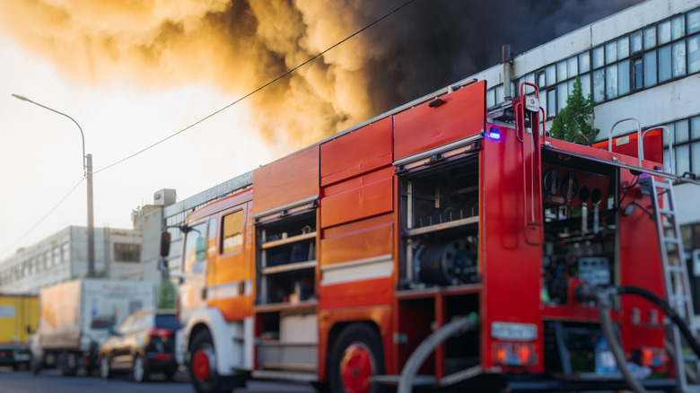 A firetruck stationed outside of an apartment building billowing with smoke.