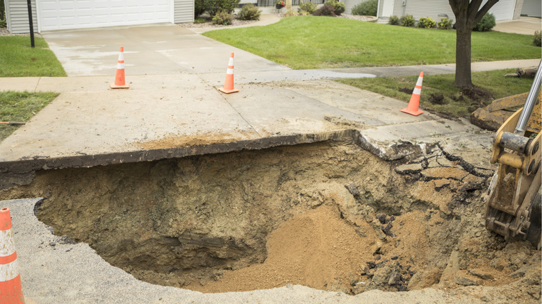 A large sinkhole at the end of a residential driveway.