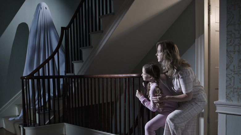 A mother and daughter peering around the corner at a ghost on the stairs.