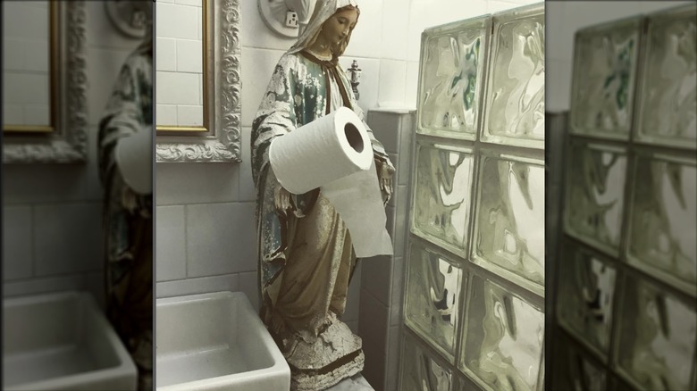 religious statue in bathroom with toilet paper