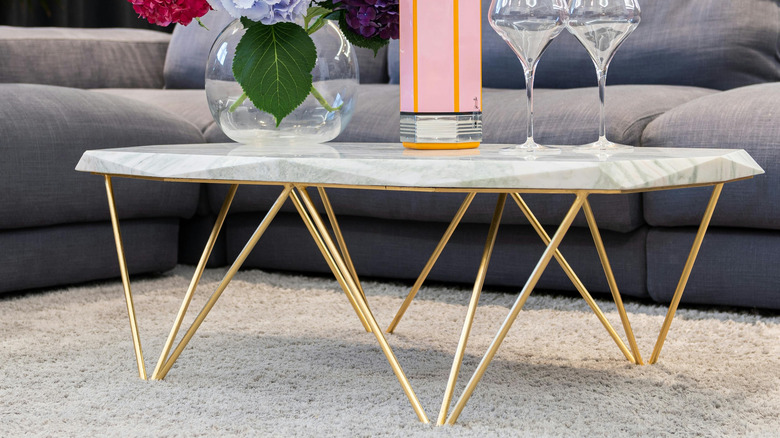 table with marble top and gleaming gold legs with quirky decoration, flower vase and wine glasses on it