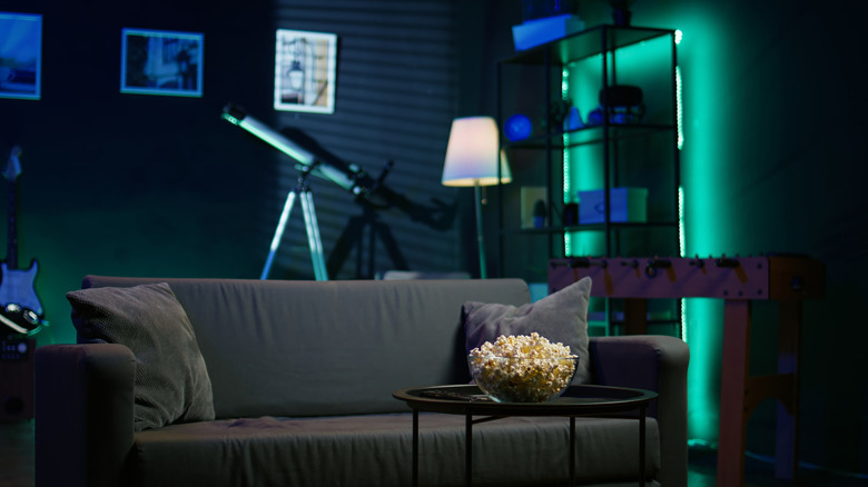 Gray sofa in living room with bowl of popcorn and bookshelf backlit by neon lights